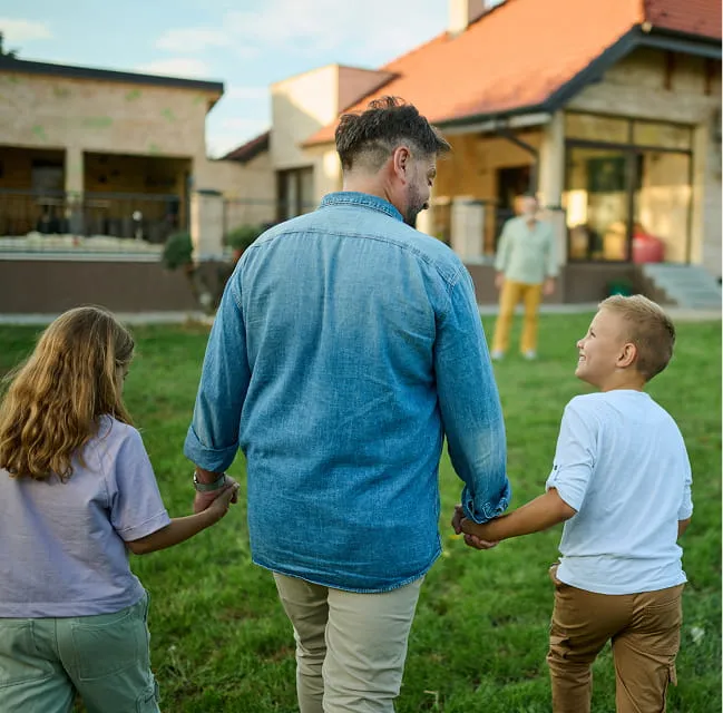 A parent holding hands with two children while walking toward a family home