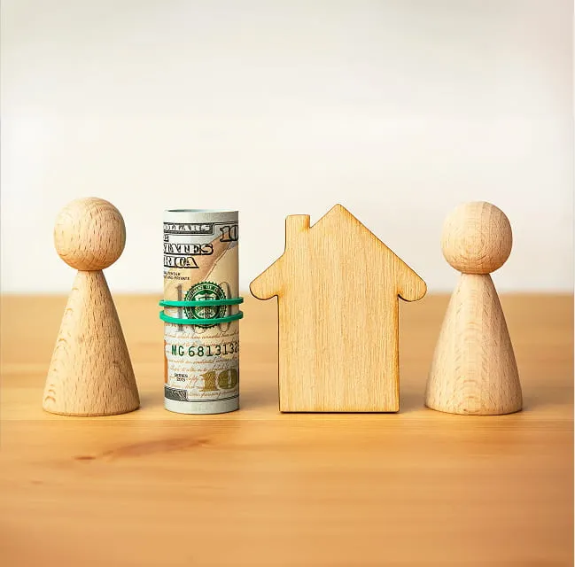 Wooden figures, a model house, and rolled currency representing home financing and property investment