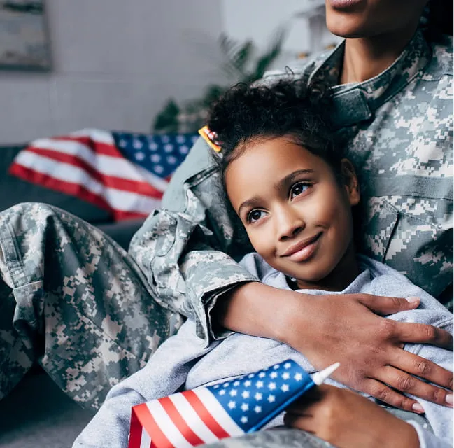 A child resting with a military parent at home while holding a small American flag