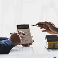 Hands using a calculator and pointing at documents next to a model house for mortgage and home loan planning